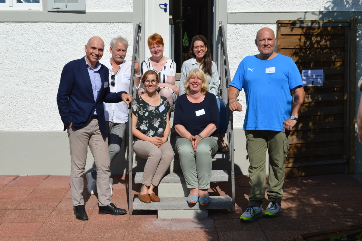 Menschen sitzen und stehen auf einer Treppe vor einem Haus.